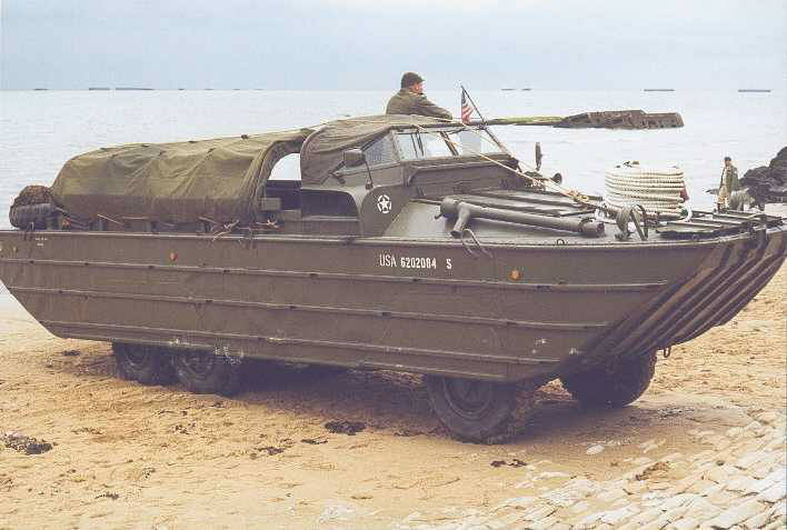 DUKW 353. C'est la version amphibie du GMC avec mme moteur et transmission. Un dispositif accessible depuis la cabine de conduite permet de faire varier la pression des pneumatiques. Remarquez  l'horizon les vestiges des caissons Phoenix, brise-lames du port artificiel d'Arromanches.